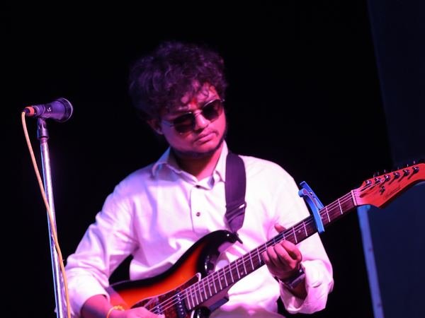 A guitarist in white playing an electric guitar on stage at a music programme at Amartarangini, Haridwar